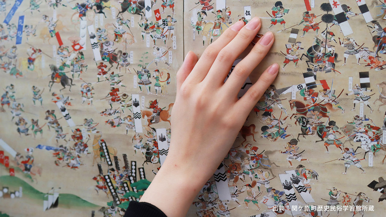 拡大画像：「ENTOUCHABLE MUSEUM -超さわれる美術館-」の体験イメージ画像です。 「関ケ原合戦図屏風」の絵に触れ、音や振動を感じる様子を再現しています。