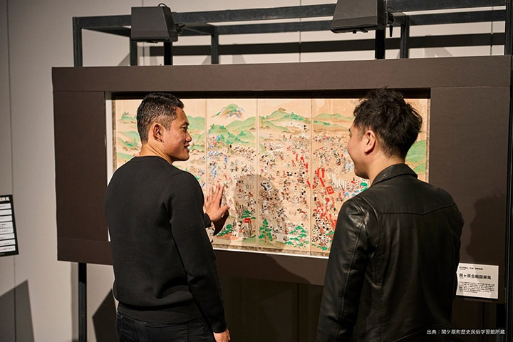 写真：大きな「関ケ原合戦図屏風」の前で、作品に触れる若生選手、ともに戦いの音やセリフに耳を傾ける澤田