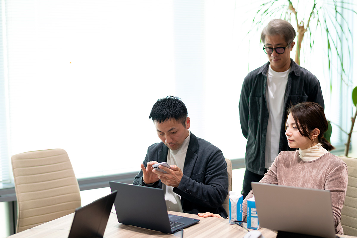 写真：スマートフォンを操作する川嶋選手と、それを見守るアクセシビリティプロジェクトメンバー2名